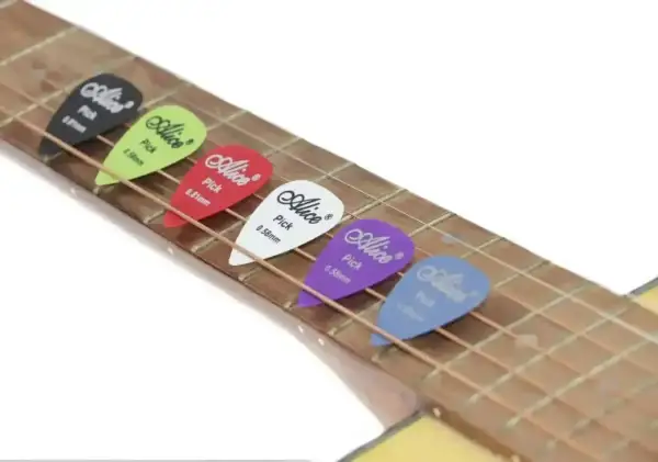 Kolorowe kostki do gry na gitarze Alice leżą na strunach. Każda kostka ma inny kolor i grubość.
