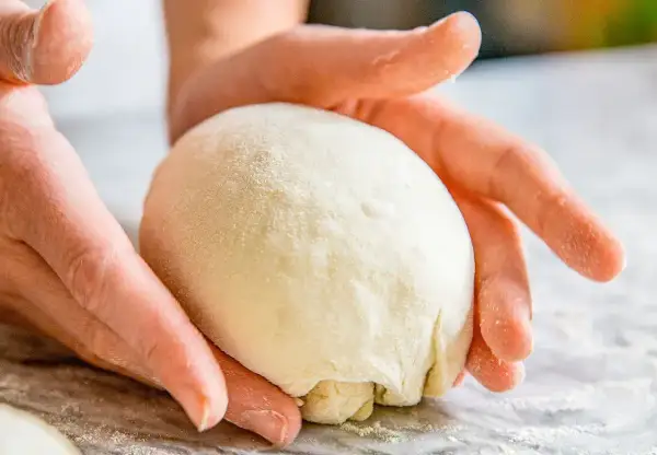Hände formen einen Teigball auf einer bemehlten Oberfläche.
