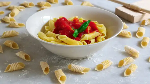 Garganelli alla contadina in una ciotola bianca, con pasta fresca sparsa sul piano di lavoro.
