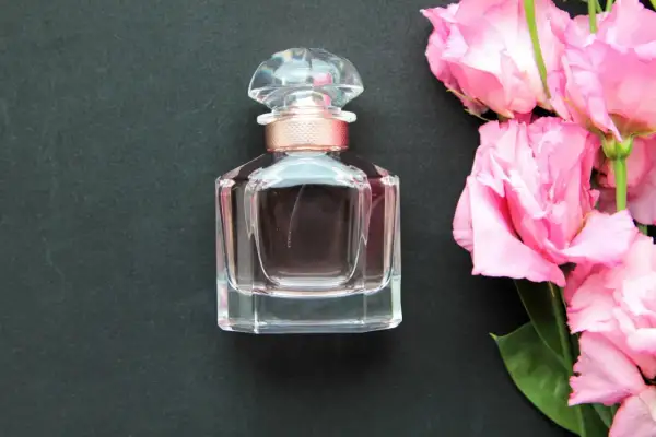 Elegancka buteleczka wody toaletowej obok bukietu różowych kwiatów. Wybór między wodą toaletową a wodą perfumowaną zależy od preferencji.