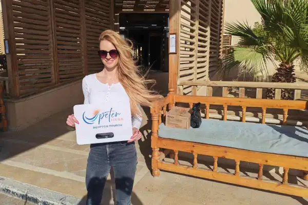 Frau in Hurghada Kleidung, mit Sonnenbrille, hält ein Schild von Peter Tours. Sie trägt Jeans und ein weißes Oberteil.
