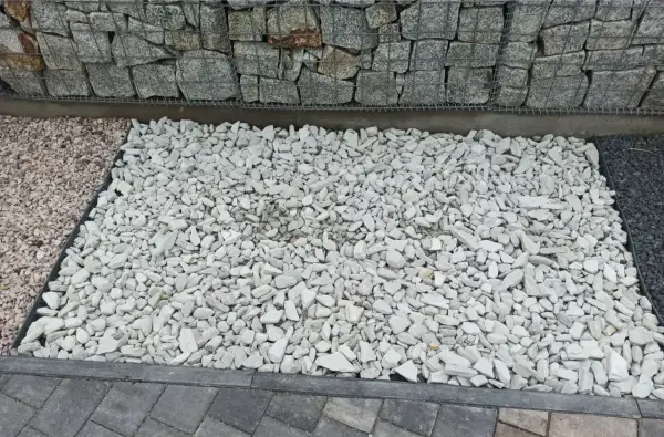 Biały grys, czyli drobne, łamane kamienie, tworzy jasną powierzchnię obok gabionów i ciemniejszego kamienia.