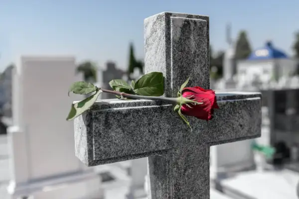 Czerwona róża na kamiennym krzyżu. Cichy symbol pochówku bez pogrzebu, samotne pożegnanie na cmentarzu.