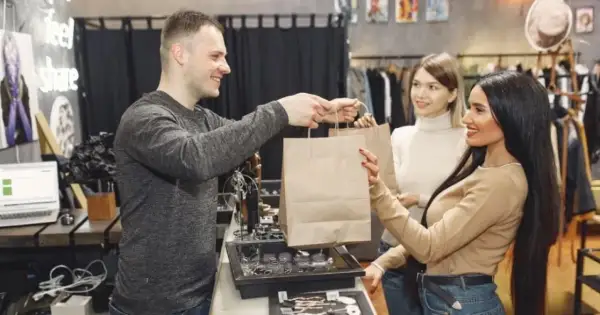 Hombre entrega bolsas de compras a dos mujeres en una tienda.