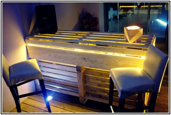 Bancone bar fai da te con pallet, illuminazione a LED e sgabelli. Un'idea creativa per un angolo bar moderno.