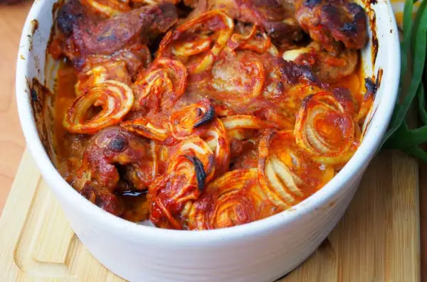 Pieczona karkówka z cebulą w sosie pomidorowym w naczyniu żaroodpornym.