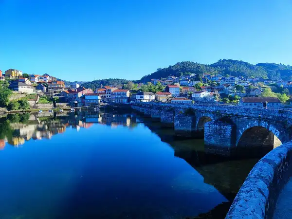 Puente de piedra en Ponte Sampaio, con casas reflejándose en el río azul bajo un cielo despejado.