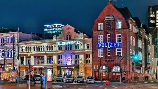 Polizeigebäude und St. Pauli Theater in Hamburg bei Nacht, mit leuchtenden Schildern und Autos.