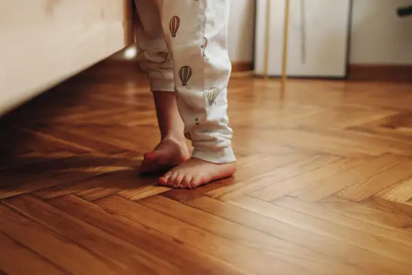 Bambino con pigiama a mongolfiere sui piedi nudi su un parquet lucido, pronto per scoprire come pulire il parquet dopo i lavori.