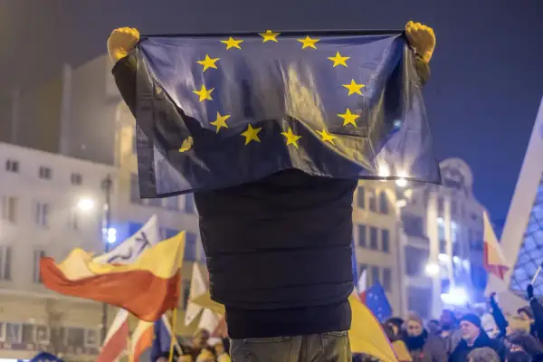 Osoba trzyma flagę UE, symbol jedności, która powstała w 1993 roku. W tle widać inne flagi i tłum ludzi.
