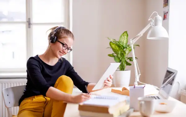 Junge Frau mit Kopfhörern und Brille lernt am Tablet für ihr **vollzeit studium**. Sie schreibt Notizen in ein Heft.