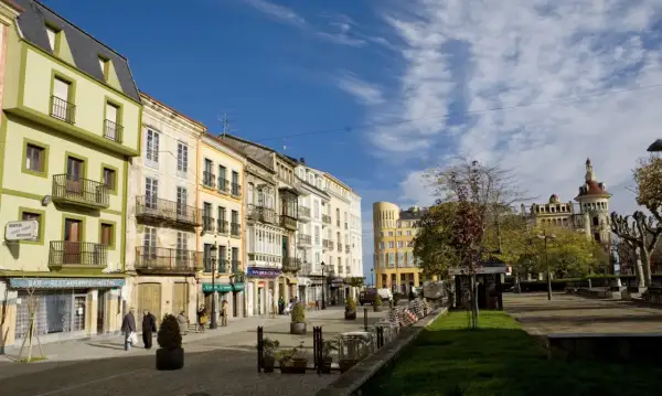 Paseo por el casco antiguo de Ribadeo que ver: fachadas coloridas, balcones de hierro y un cielo azul con nubes.