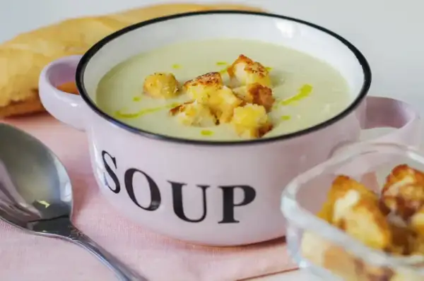 Kremowa zupa z selera naciowego z grzankami w różowej miseczce z napisem "SOUP".