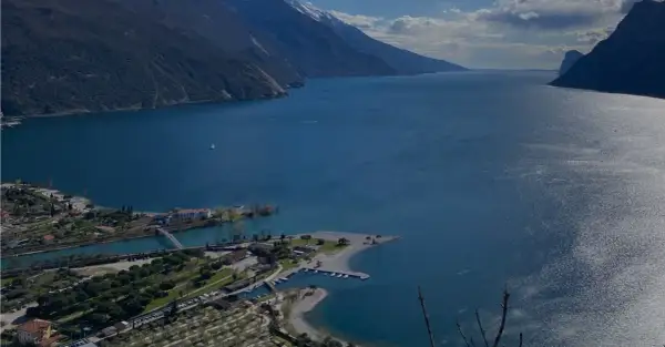 Vista panoramica del lago con montagne sullo sfondo. In primo piano, un lido e un camping vicino ad Arco.
