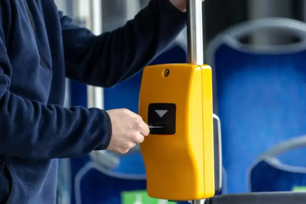 Osoba wkłada kartę do żółtego kasownika w autobusie, pokazując, jak kupić bilet.