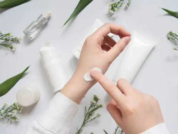 Eine Hand testet eine weiße Creme, umgeben von Pflegeprodukten und zarten Blüten. CI 45410.