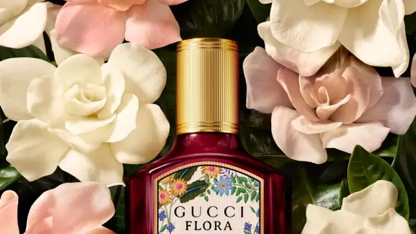 Perfumy Gucci by Gucci Flora w otoczeniu delikatnych kwiatów. Złota nakrętka i bogata etykieta z motywem roślinnym.