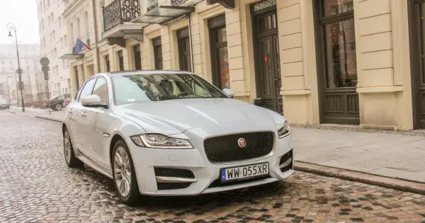 Biały Jaguar XF 3.0 Diesel na brukowanej ulicy przed kamienicą.