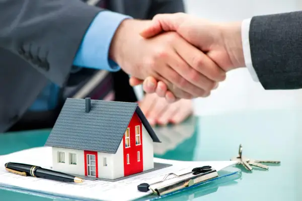 Accordo per un contratto di locazione: stretta di mano su un modello di casa, penna e chiavi.