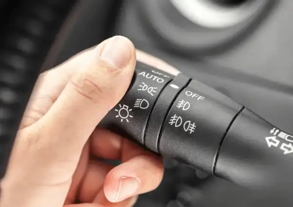 Dłoń kierowcy reguluje przełącznik świateł: auto, światła mijania, światła dzienne, przeciwmgielne.