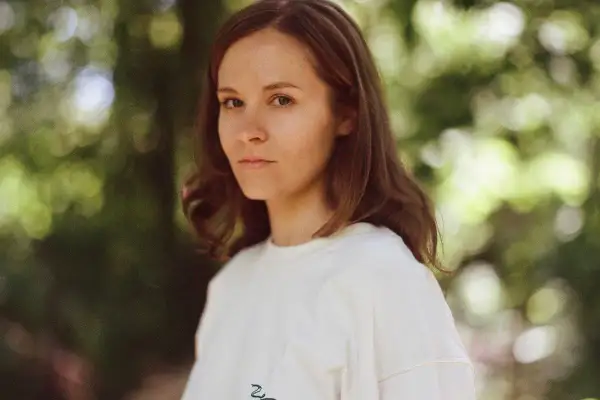 Hania Rani Esja, artystka o hipnotyzującym spojrzeniu, w białej bluzie na tle zieleni.