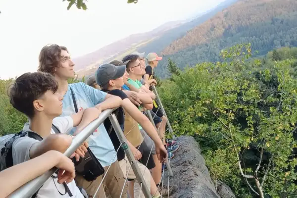Grupa młodych ludzi podziwia widok z góry. To właśnie jest co to trekking – podróżowanie pieszo przez góry, odkrywanie piękna natury.