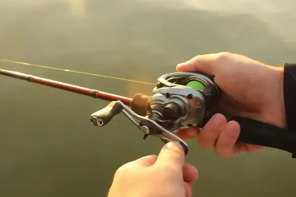 Dłonie trzymają wędkę z kołowrotkiem, gotowe do rzutu. Precyzyjne **casting spinning** to klucz do sukcesu.