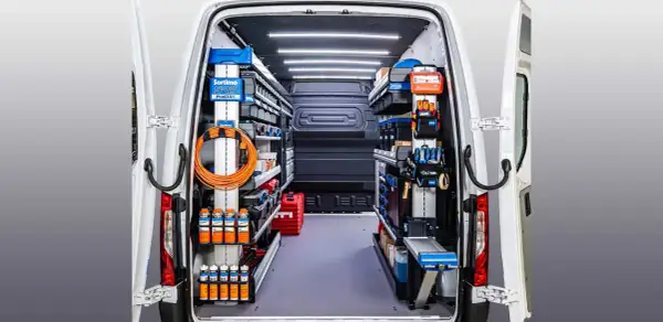 Interior de un autobús camperizado en España, organizado con estanterías y herramientas.