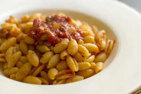 Malloreddus alla campidanese, pasta sarda con sugo di pomodoro e salsiccia, serviti in un piatto bianco.