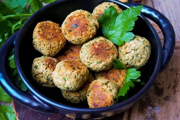 Köstliche Falafel, frisch zubereitet nach einem einfachen falafel rezept, liegen in einer schwarzen Schüssel, garniert mit Petersilie.
