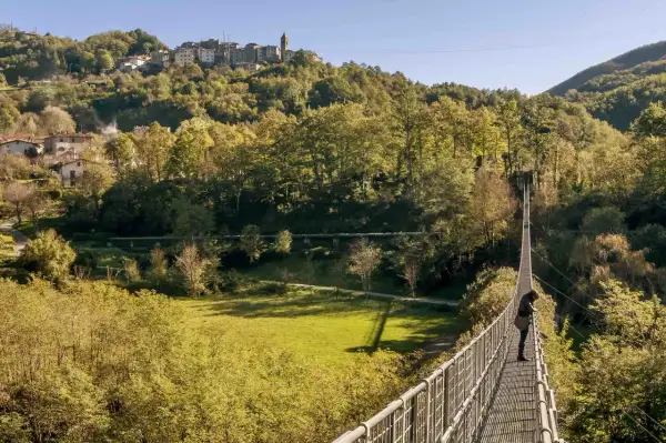 Una persona osserva il panorama dal ponte sospeso delle Ferriere, con un borgo arroccato sulla collina sullo sfondo.