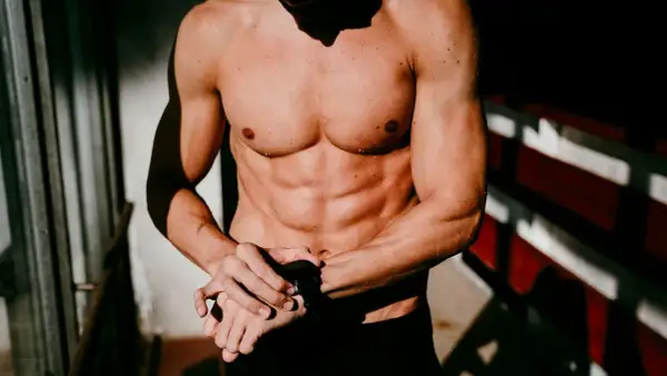 Ein Mann mit einem definierten Sixpack und nasser Haut blickt auf seine Sportuhr.