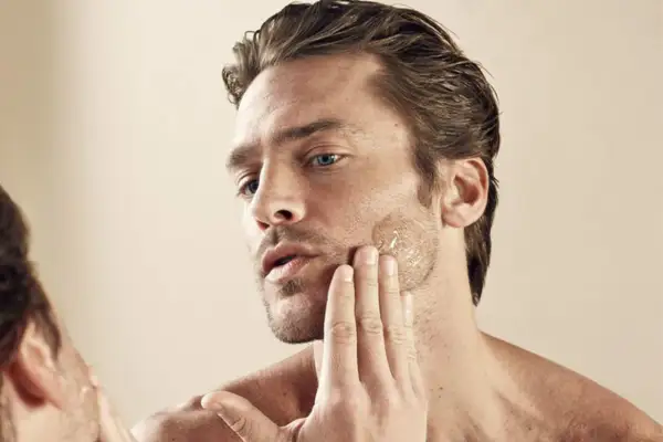 Un homme applique un soin sur sa barbe qui pique, sa main caresse sa joue.