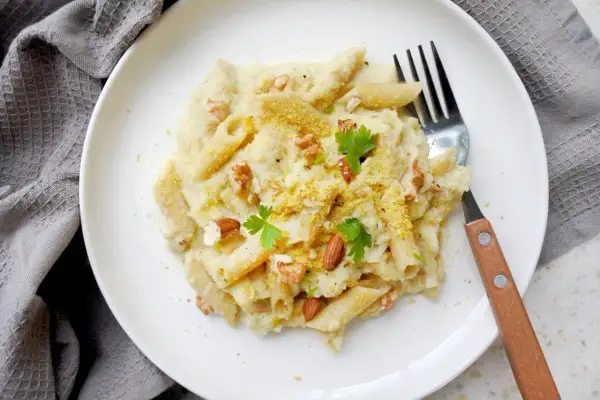 Penne z kremowym sosem z kalafiora, orzechami i natką pietruszki. Pyszny makaron z kalafiorem na białym talerzu.