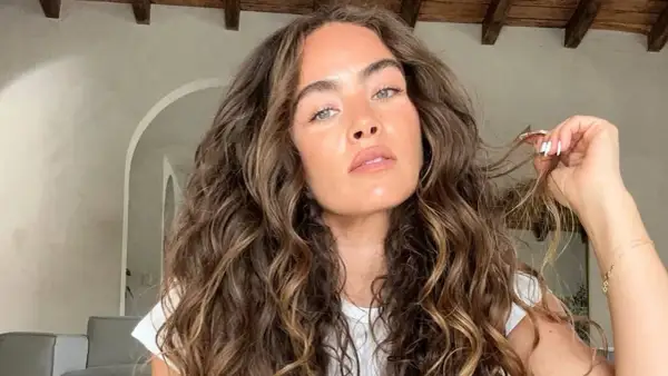 Mujer con un espectacular pelo rizado castaño, con reflejos dorados, acariciando un mechón.