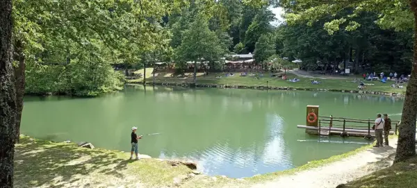 Un ragazzo pesca sul lago Pontini, mentre altre persone si rilassano sull'erba.