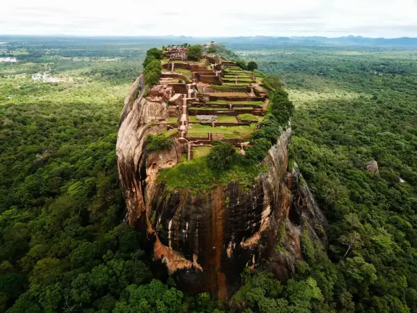 Imponerande ruiner på toppen av en klippa, som en fästning. En vy som påminner om Adams Peak, omgiven av frodig djungel.