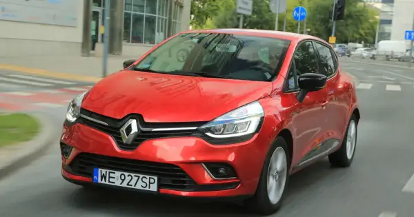 Czerwony Renault Clio 3 1.2 benzyna w ruchu miejskim. Kierowca w okularach przeciwsłonecznych.
