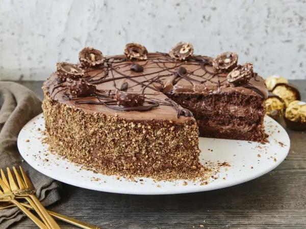 Schokoladentorte mit Ferrero Rocher verziert, die Seiten sind mit gehackten Nüssen bedeckt. Ein Stück fehlt, was Lust auf mehr macht.