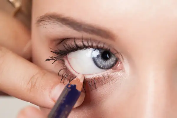 Una mano applica una matita bianca per illuminare la rima interna dell'occhio, un trucco per ingrandire lo sguardo.