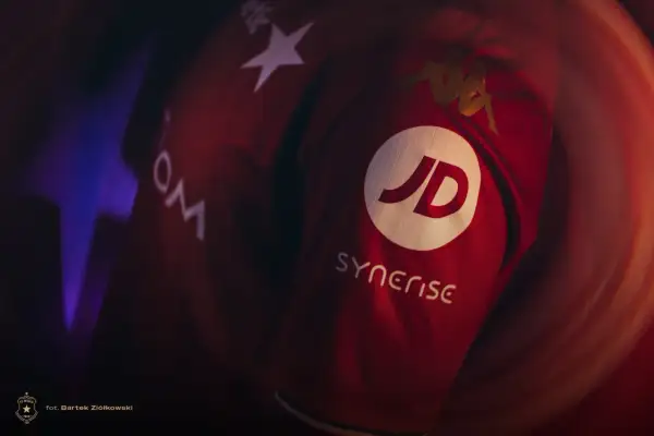 Czerwona koszulka Wisły Kraków z logo JD i Synerise. Widoczne też logo Kappa i gwiazda.