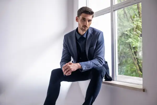 Elegancki mężczyzna w granatowej koszuli i marynarce, zastanawia się, jakie spodnie do niebieskiej koszuli będą najlepszym wyborem.