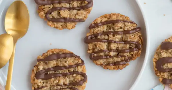 Nyttiga havrekakor utan socker, dekorerade med choklad, ligger på en vit tallrik bredvid guldfärgade skedar.
