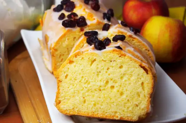 Wilgotna babka na oleju z kakao, polana lukrem i posypana żurawiną, obok jabłek.