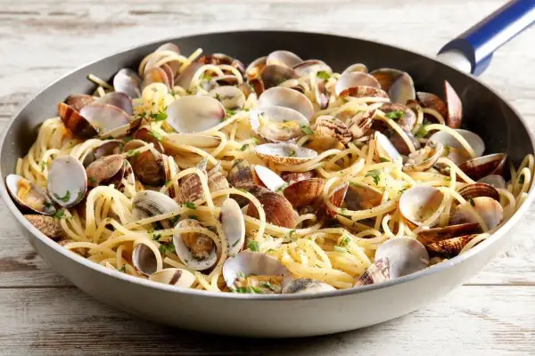 Un piatto invitante di spaghetti con le vongole, condito con prezzemolo fresco, servito in una padella su un tavolo di legno.