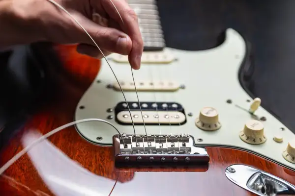 Dłoń naciąga nowe struny w gitarze elektrycznej, przygotowując ją do gry.
