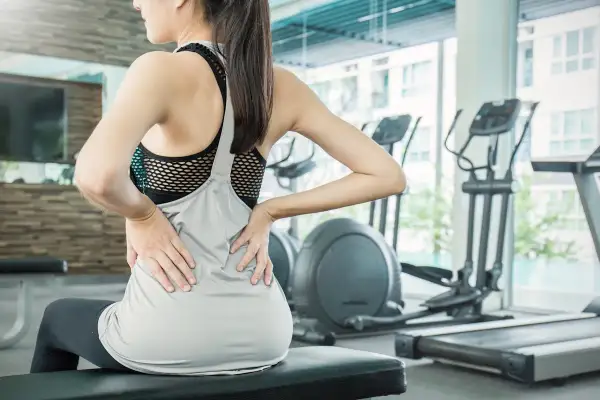 Donna in palestra con le mani sulla schiena, soffre di mal di schiena. Attenzione agli esercizi da evitare in palestra per il mal di schiena.