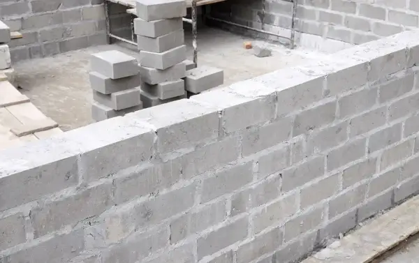 Budowa fundamentów z bloczków betonowych. Stos świeżo ułożonych bloczków betonowych fundamentowych obok wznoszonej ściany.