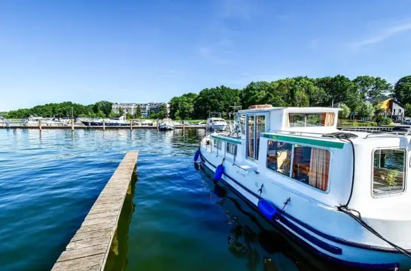 Ein Hausboot liegt im Hafen an der Mecklenburgischen Seenplatte. Ein Holzsteg führt ins klare Wasser.