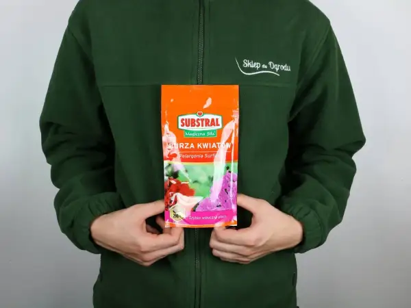 Opakowanie nawozu Substral Burza Kwiatów z pelargoniami, trzymane przez osobę w zielonej bluzie.